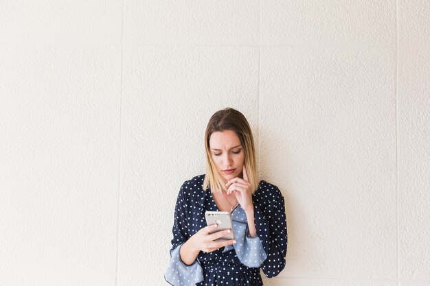 Young woman using mobile phone in front of wall