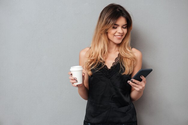 携帯電話と一杯のコーヒーを保持している若い女性