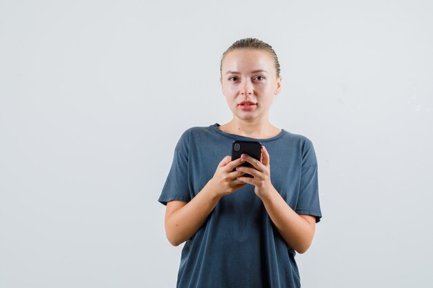 Молодая женщина с помощью мобильного телефона, глядя в серой футболке
