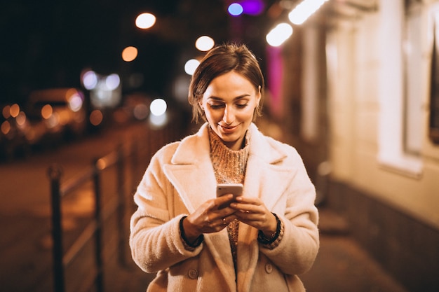 夜の街の外の電話を使用して若い女性