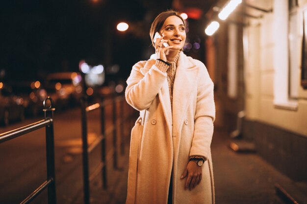 Young woman using phone outside the night street