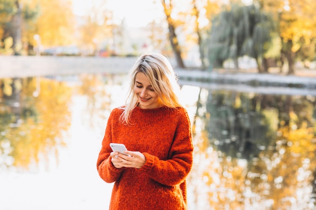 Young woman using phone in park by the lake