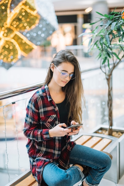 無料写真 ショッピングモールのベンチにスマートフォンを使用して若い女性