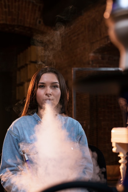 Free photo young woman vaping from a hookah in a bar