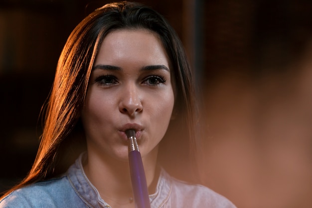 Free photo young woman vaping from a hookah in a bar