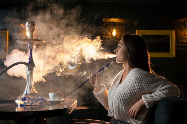 Foto gratuita giovane donna che svapa da un narghilè in un bar