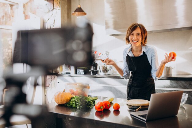 若い女性のビデオブロガー、キッチンで料理と撮影