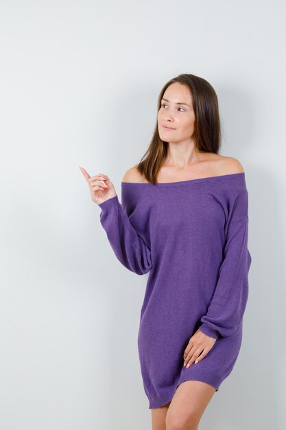 Young woman in violet shirt pointing to side and looking focused , front view.