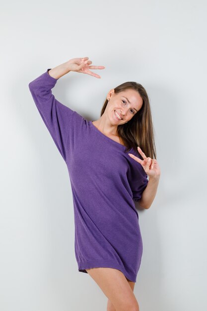 Молодая женщина в фиолетовой рубашке показывает v-знак и выглядит счастливым, вид спереди.