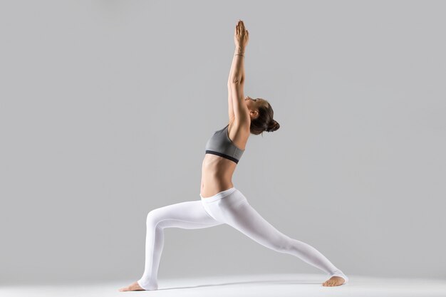 Young woman in Virabhadrasana I pose, grey studio background