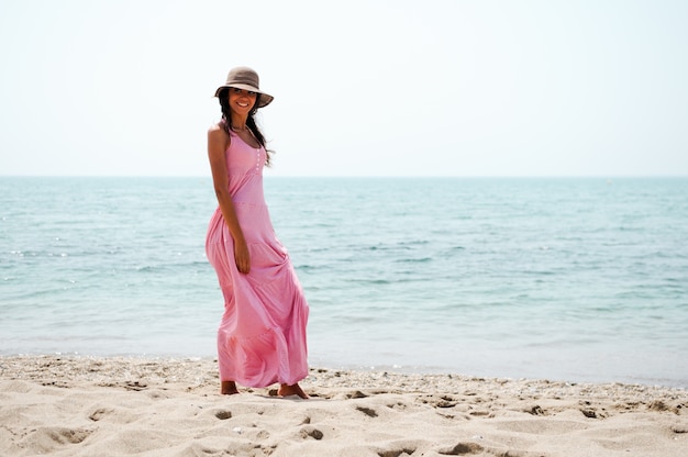 핑크 드레스와 함께 해변을 따라 걷는 젊은 여성