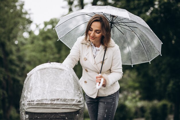 雨の日の傘の下でベビーカーと一緒に歩いている若い女性