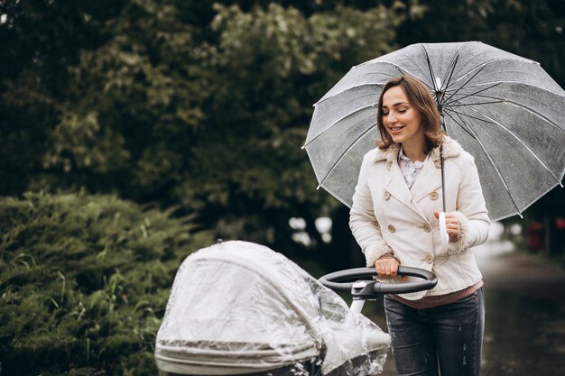 Young woman walking with baby carriage under the umbrella in a raint weather