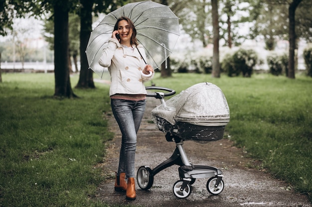 Молодая женщина гуляет с коляской под зонтиком в дождливую погоду