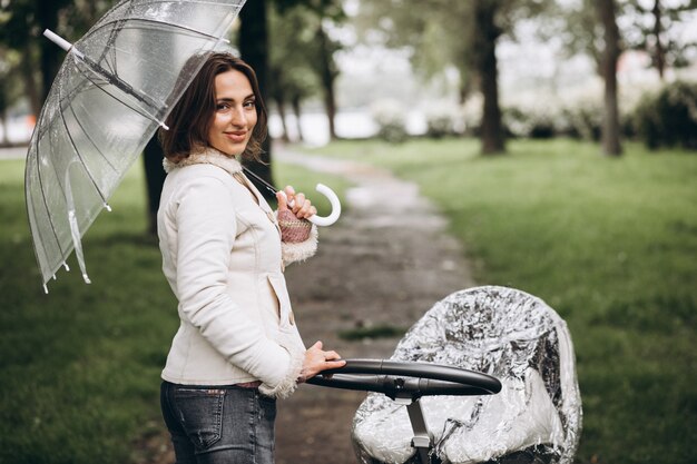 Young woman walking with baby carriage under the umbrella in a raint weather