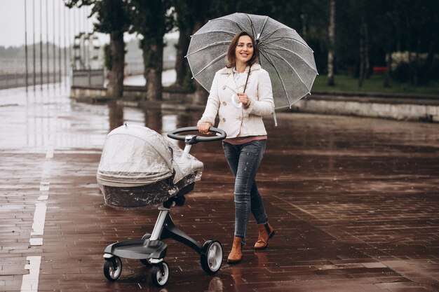 雨の日の傘の下でベビーカーと一緒に歩いている若い女性