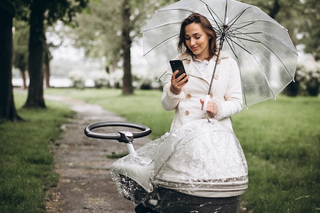 雨の日の傘の下でベビーカーと一緒に歩いている若い女性