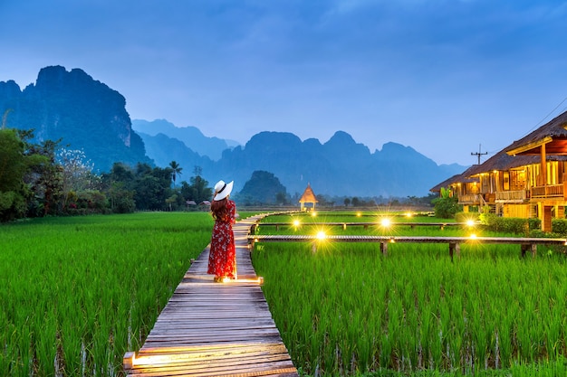 Young woman walking on wooden path with green rice field in Vang Vieng, Laos.