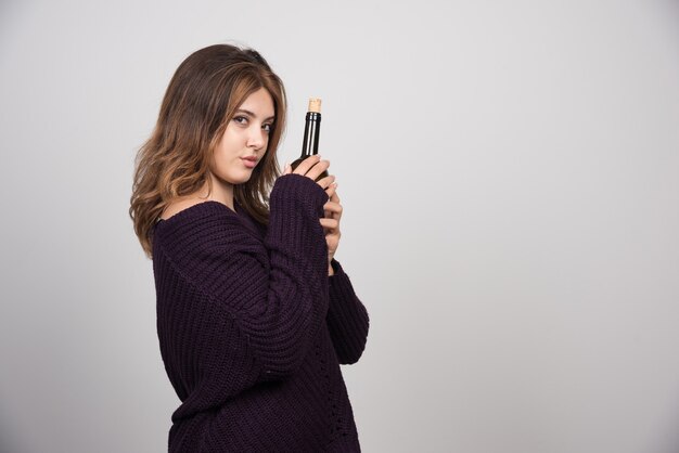 Young woman in warm knitted sweater holding a bottle of wine .