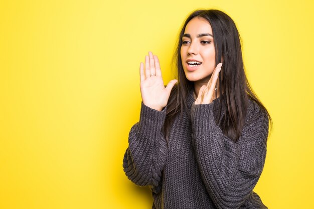 Young woman in warm sweater scream isolated on yellow