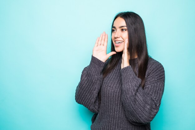 Young woman in warm sweater screaming on blue