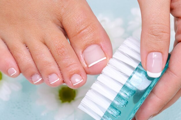 Молодая женщина моет и чистит ногти на ногах в воде с помощью очищающей щетки.