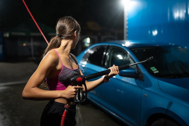 Young woman washing blue car at car wash