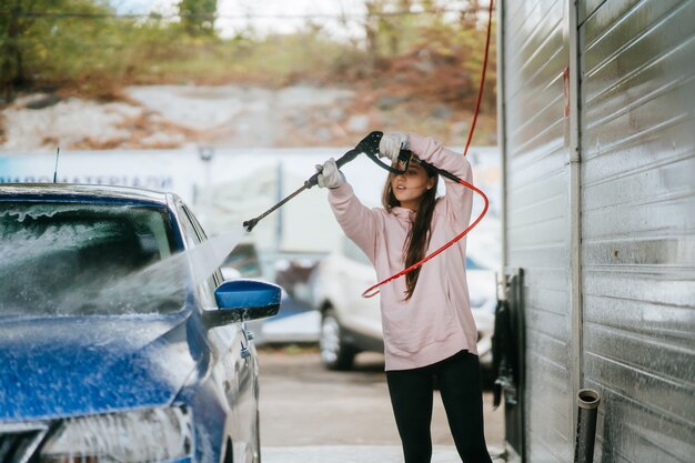 Young woman washing blue car at car wash