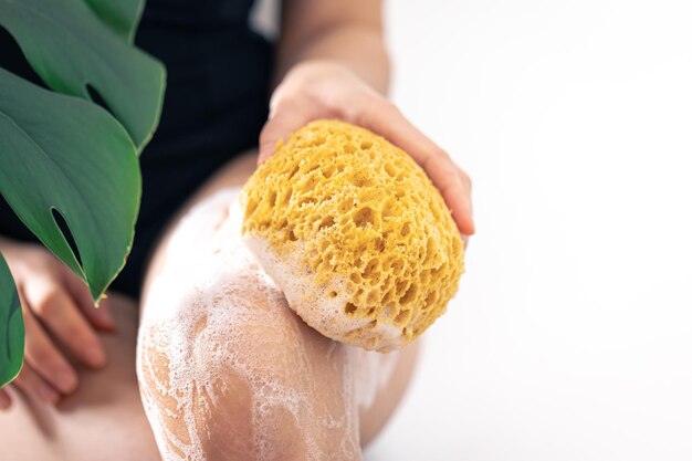 黄色いスポンジと石鹸の泡で足を洗う若い女性