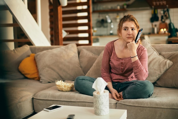 Free photo young woman watching sad movie on tv in the living room