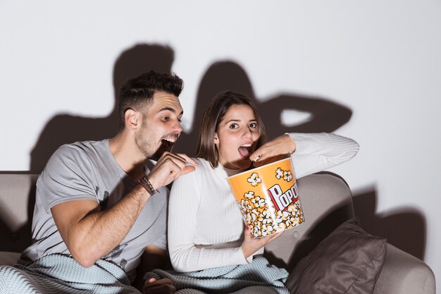 Young woman watching TV and eating popcorn near man on settee