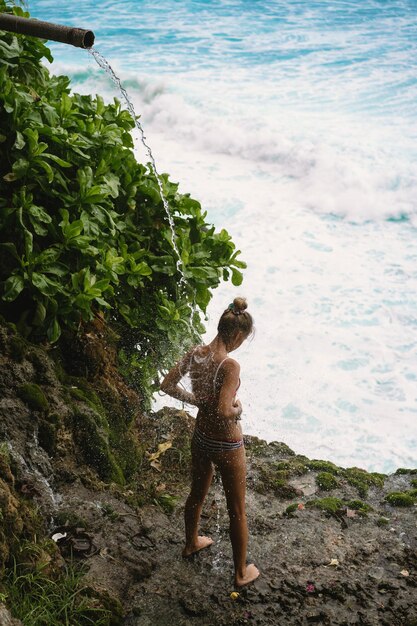 自然と一体となった崖の上の滝の下の若い女性