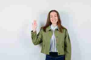 無料写真 シャツ、ジャケット、陽気に見える、正面図で挨拶のために手を振っている若い女性。