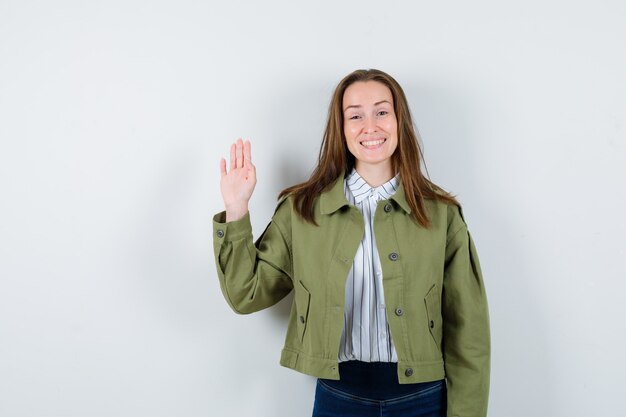 Foto gratuita giovane donna agitando la mano per salutare in camicia, giacca e guardando allegra, vista frontale.