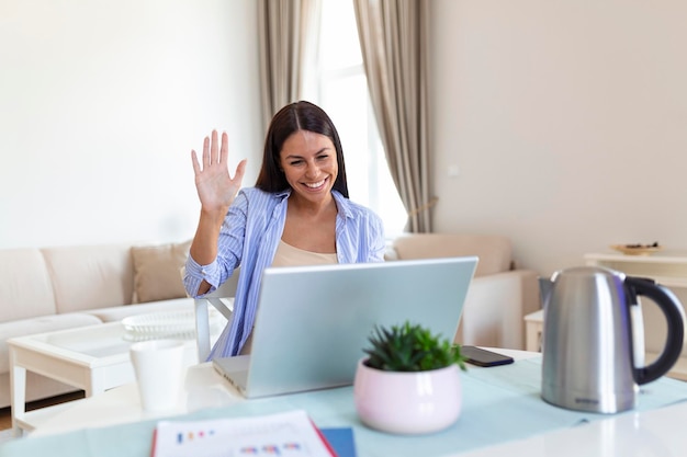 Free photo young woman waving at laptop and talking to her friends via video call girl student talking by video conference call female teacher trainer tutoring by webcam online training ecoaching concept