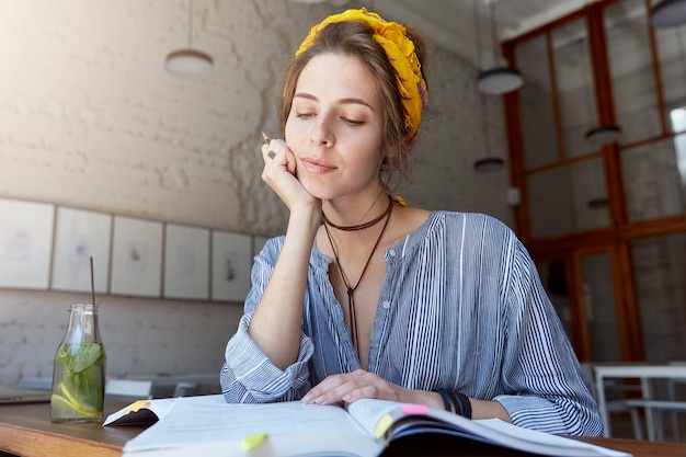 Free photo young woman wearing bandana and studying in cafe