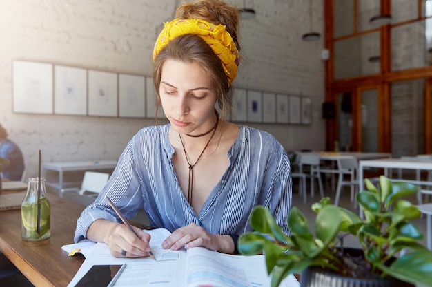 Young woman wearing bandana and studying in cafe