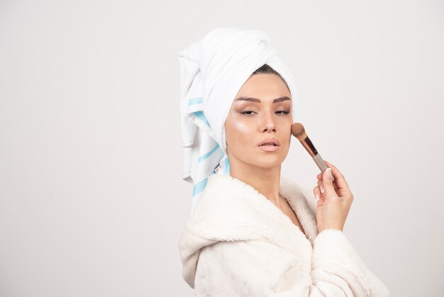 Young woman wearing bathrobe and towel use tassel for make-up.