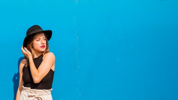 Foto gratuita giovane donna che indossa cappello nero in piedi su sfondo blu