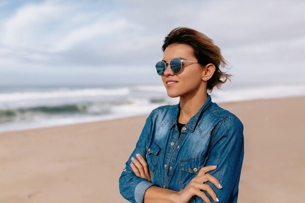 Young woman wearing denim shirt with sunglasses posing on beach