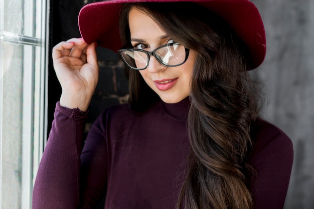 Young woman wearing eyeglasses holding hand on hat over her head