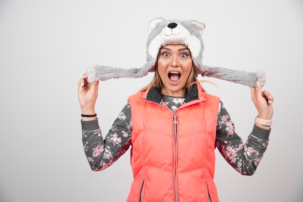 Young woman wearing funny hat on a white wall.