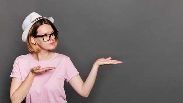 Young woman wearing hat presenting something against grey background