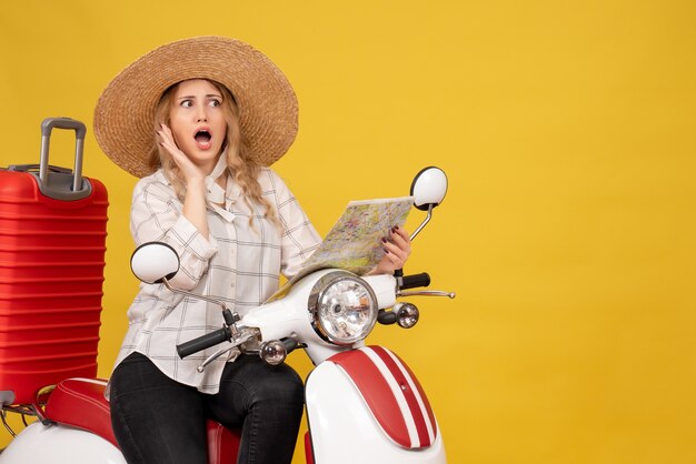 Young woman wearing hat and sitting on motorcycle and holding map listening to the last gossiping on yellow 