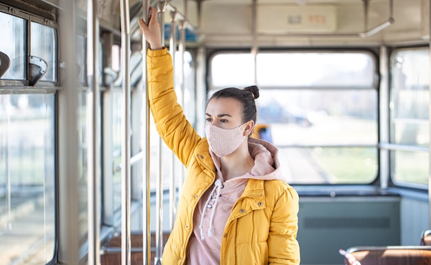 A young woman wearing a mask stands alone on empty public transport during the coronavirus pandemic