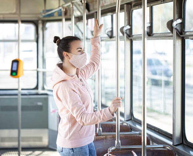 A young woman wearing a mask stands alone on public transport during the coronavirus pandemic.