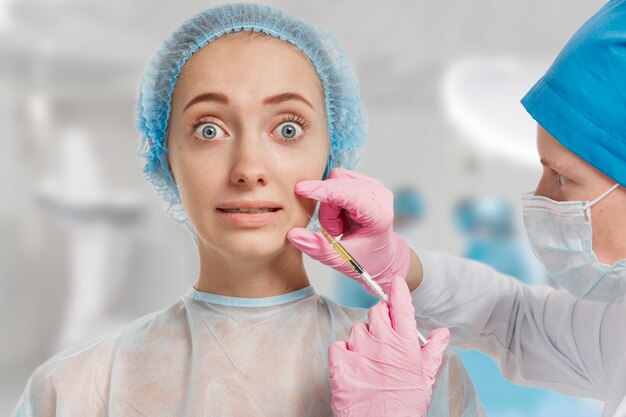 Young woman wearing medical headwear while doctor injects her face