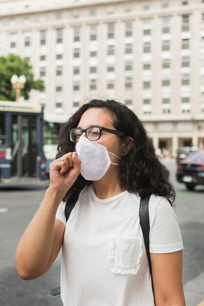 Young woman wearing a medical mask  and coughing outdoors