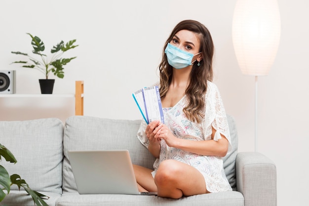 Young woman wearing a medical mask while holding plane tickets