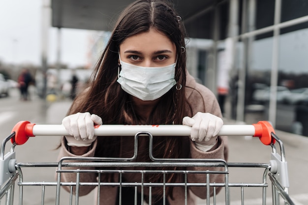 Young woman wearing protection face mask against coronavirus 2019-nCoV pushing a shopping cart.